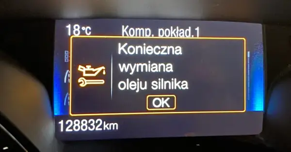 Wyświetlacz samochodowy z komunikatem "Konieczna wymiana oleju silnika" i ikoną klucza.